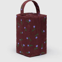 baggu dopp kit with painted purple flowers on a burgundy recycled nylon background standing on one end showing the zipper closure and loop for carrying or hanging
