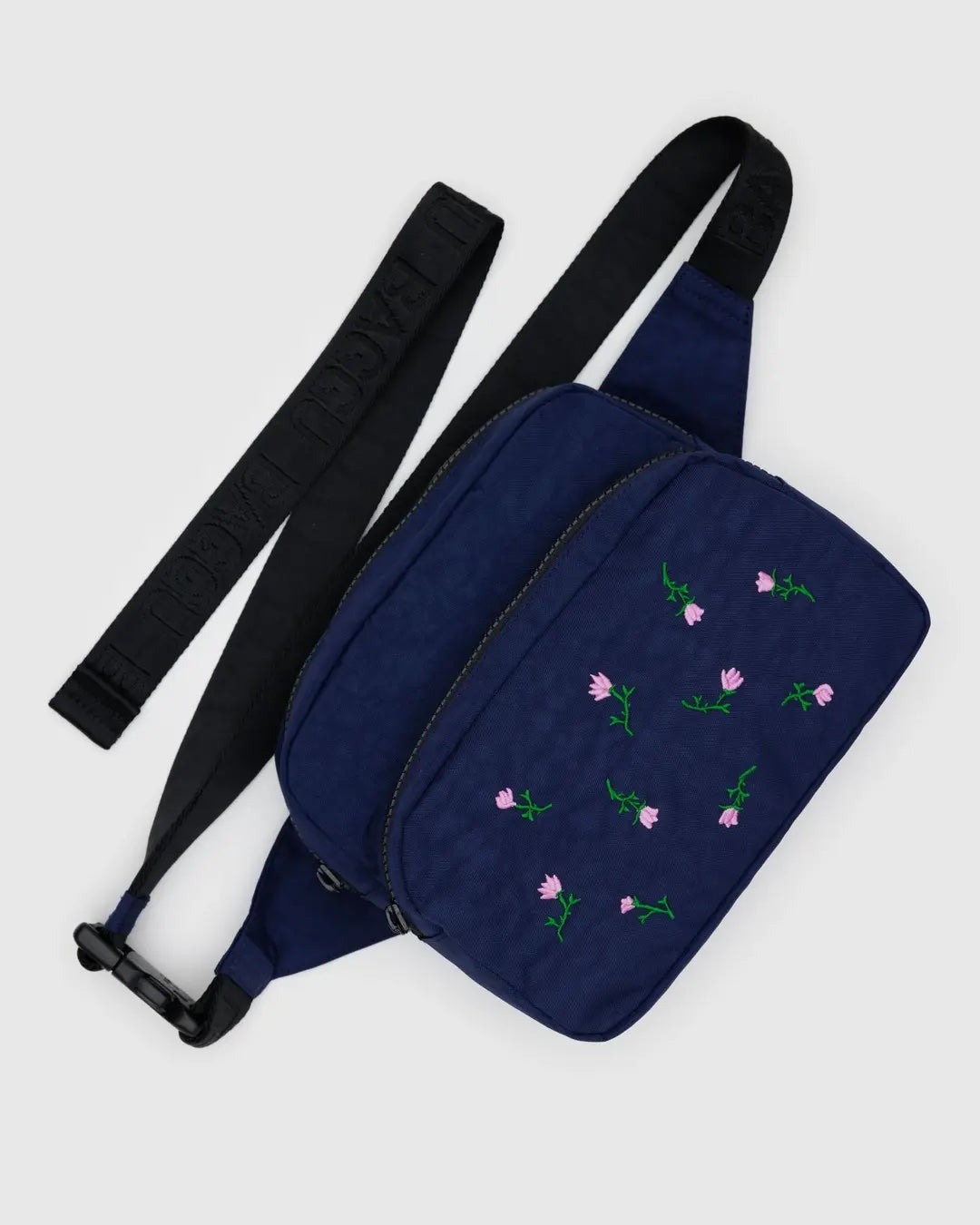 Baggu Navy blue crossbody fanny pack bag with pink wildflower embroidery and black adjustable strap on a light grey background