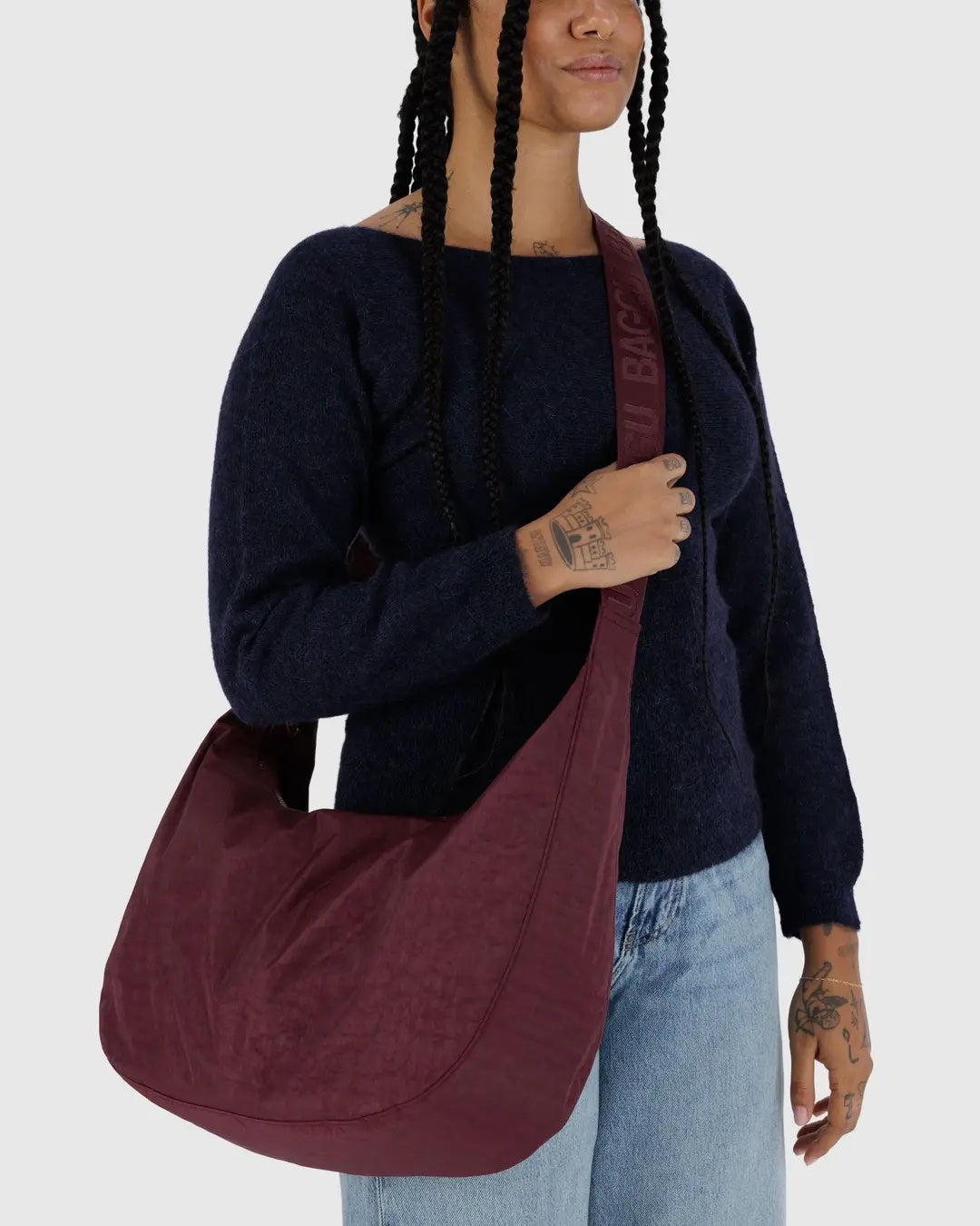 a person wearing a blue sweater and pale denim jeans is shown wearing a large Baggu crescent bag crossbody