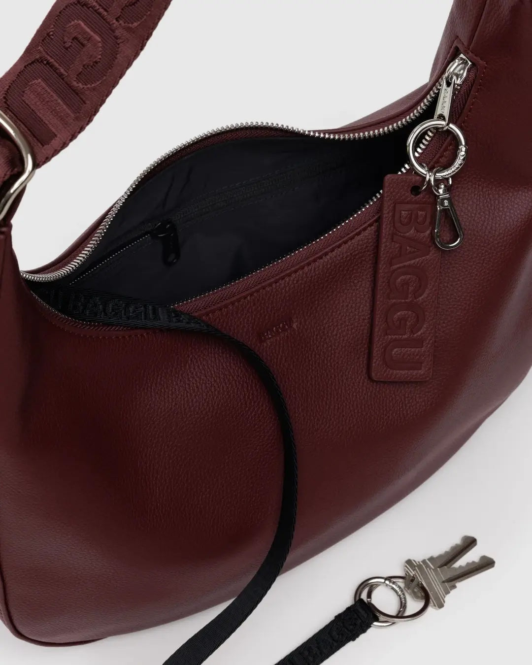 detail shot of a baggu medium recycled leather crescent bag in mahogany red showing silver metal zipper and key ring hardware, matching mahogany strap and internal key lanyard