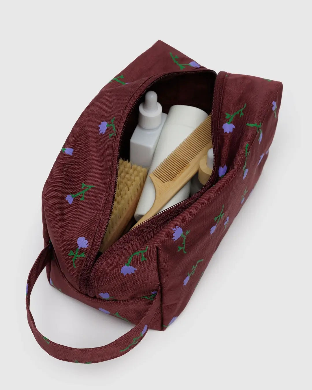 baggu painted wildflower dopp kit open on a white background holding a variety of white bottles and wooden personal care items