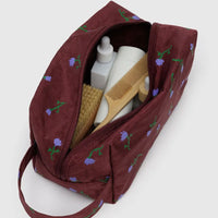 baggu painted wildflower dopp kit open on a white background holding a variety of white bottles and wooden personal care items