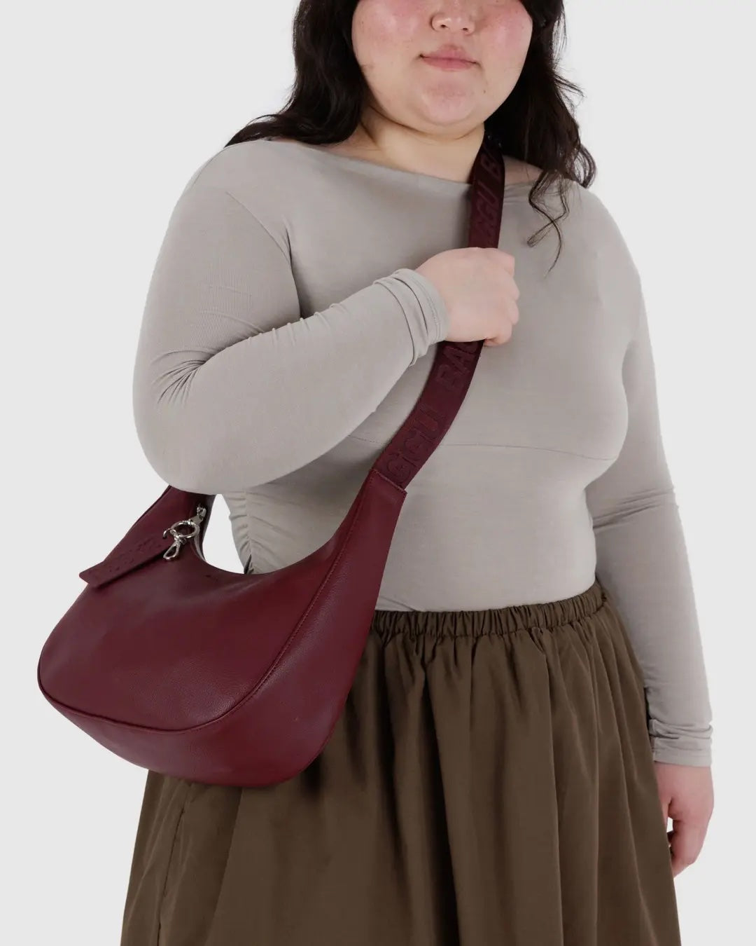 person with long dark hair, wearing grey fitted top and khaki skirt is shown with a medium baggu leather crescent bag being worn crossbody