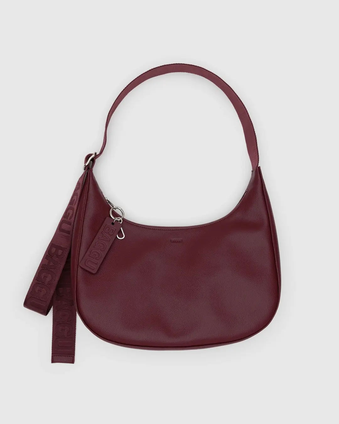 baggu medium crescent bag in mahogany made from recycled leather with matching strap and embossed key lanyard detail against a white background