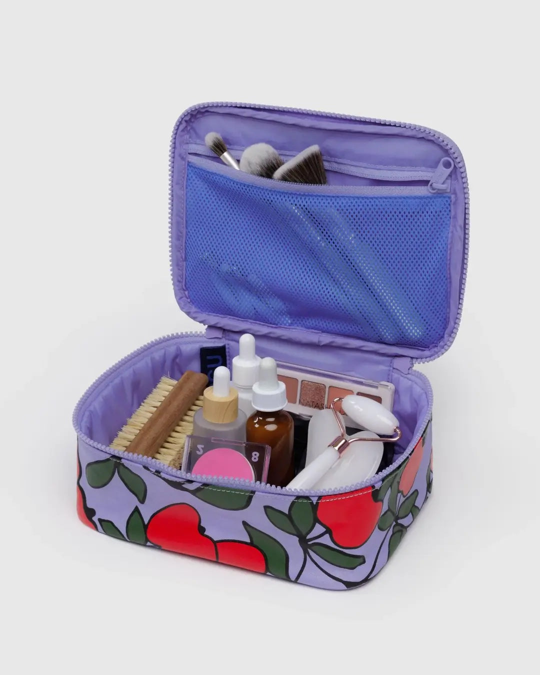 apple tree printed small baggu cosmetic case shown opened with a nail brush, rose quartz gua sha and a variety of other toiletries and cosmetics inside
