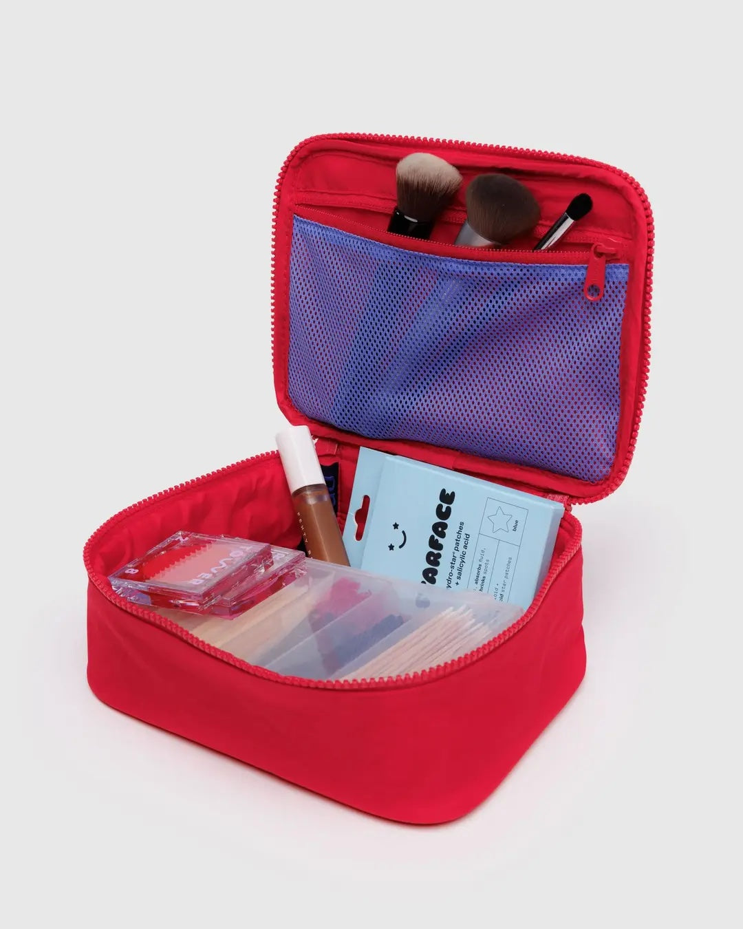 Red Baggu cosmetic bag with makeup items on a white background