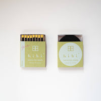 an open 8-pack of hibi mimosa incense matches in a green box on a white background. The matches are black with canary yellow tips