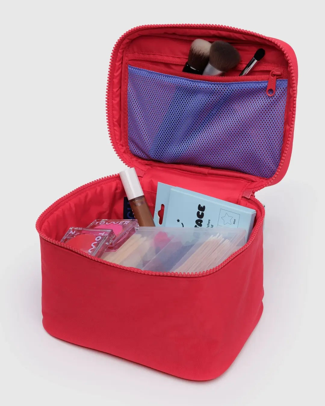 an open view of a candy apple red baggu cosmetic case showing interior pocket and a variety of cosmetics