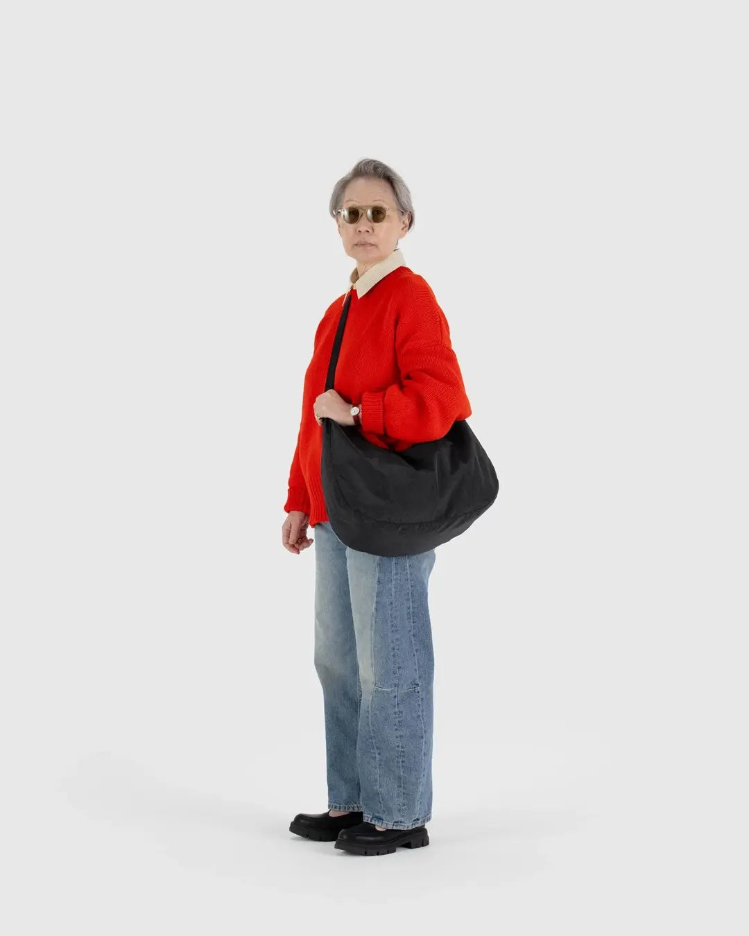 a person wearing jeans and a red sweater is shown wearing a large black baggu nylon crescent bag across their body