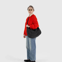 a person wearing jeans and a red sweater is shown wearing a large black baggu nylon crescent bag across their body