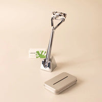Leaf Shave chrome triple blade razor in a stand with a pack of blades and used blade bank on a beige background