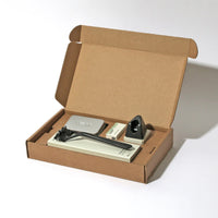 open cardboard box containing Leaf triple blade razor, blades, blade bank and razor stand on a white background