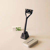 Black razor with stand and silver case on a beige background