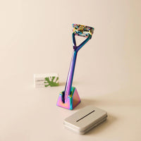 Leaf Prism coloured razor, stand, blades and used blade bank on beige background