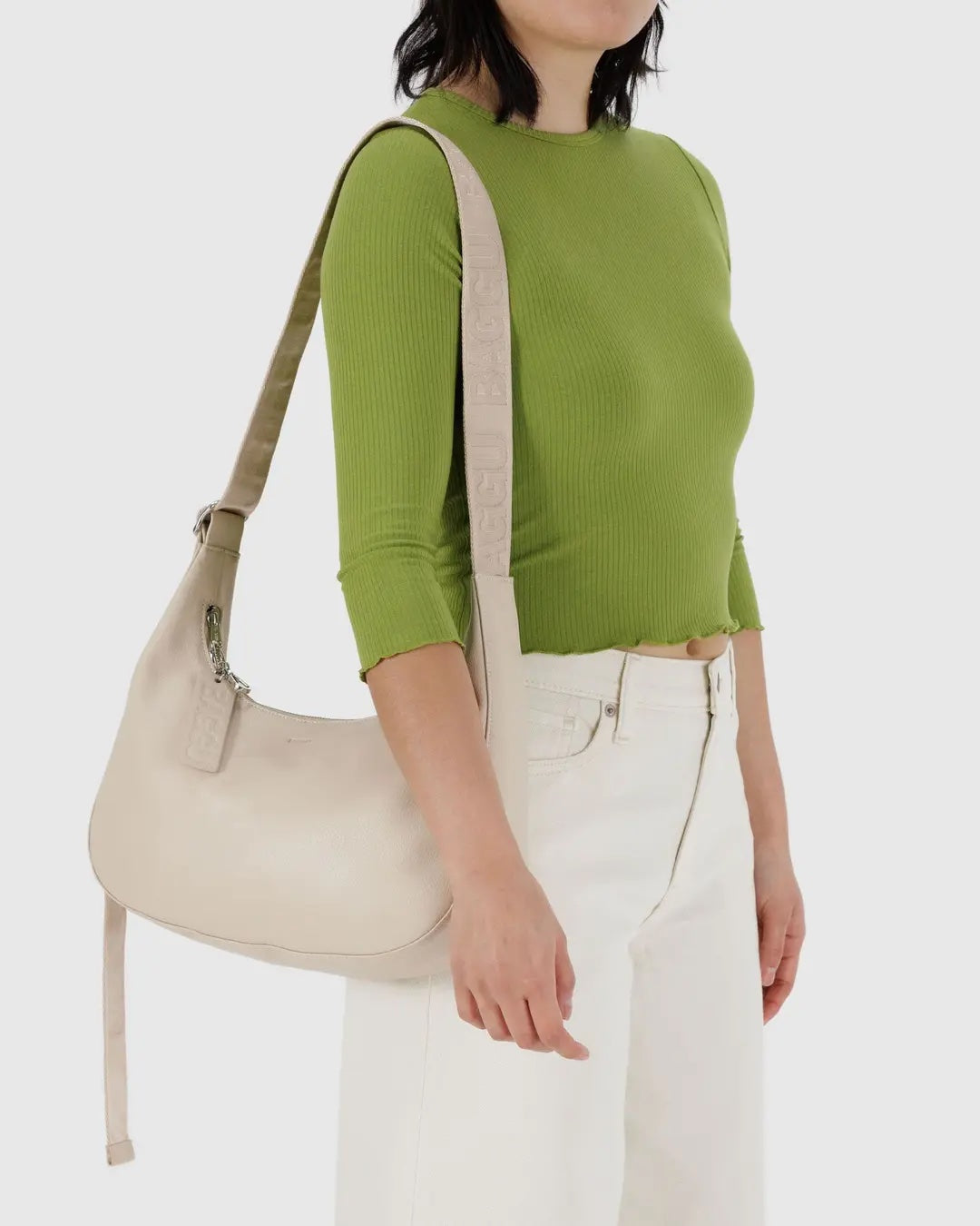 Person wearing a green sweater and white pants carrying a stone leather Baggu medium crescent on their shoulder