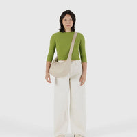 Person wearing a green top and white pants with a stone baggu leather medium crescent bag crossbody