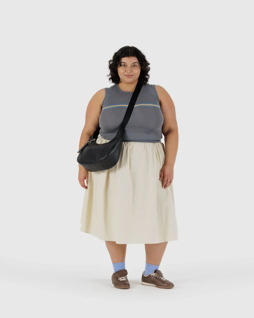 Person wearing a sleeveless top and skirt wearing a Baggu black leather crescent bag cross body on a white background