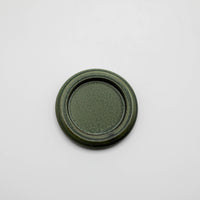 a small round green porcelain tray made for burning hibi incense matches against a white background