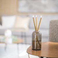 image of lit gold everlasting candles in a smokey grey vase.