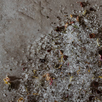 Well Kept soaking salts spilled out onto a beige stone surface showing the salts and botanicals texture