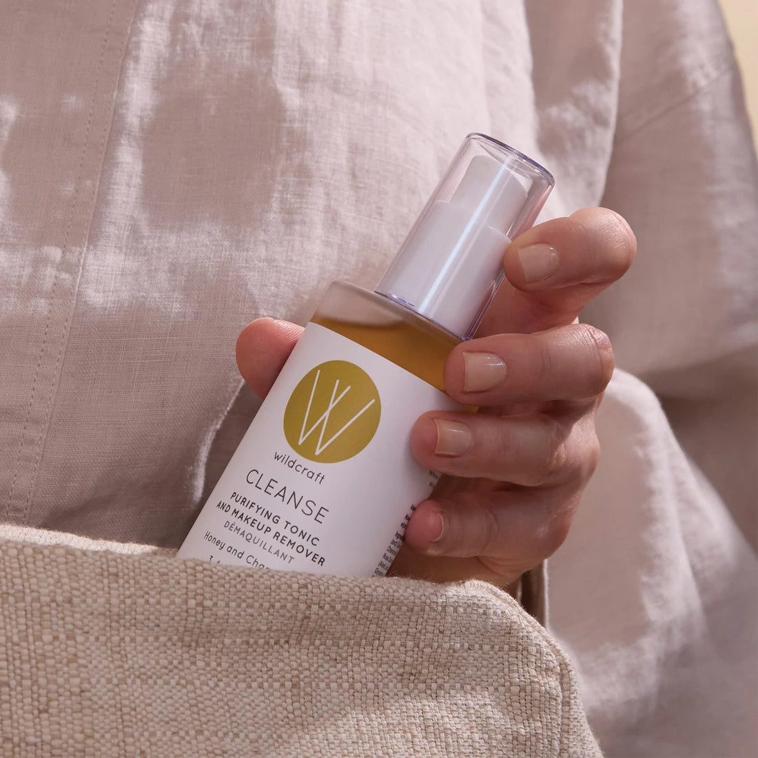 Hand holding a bottle of 'Wildcraft Cleanse' Purifying Tonic about to place it in a beige linen bag