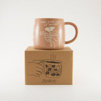 A light terracotta colour ceramic mug by People I've Loved with cream simplistic flower print and text "take good care of yourself"