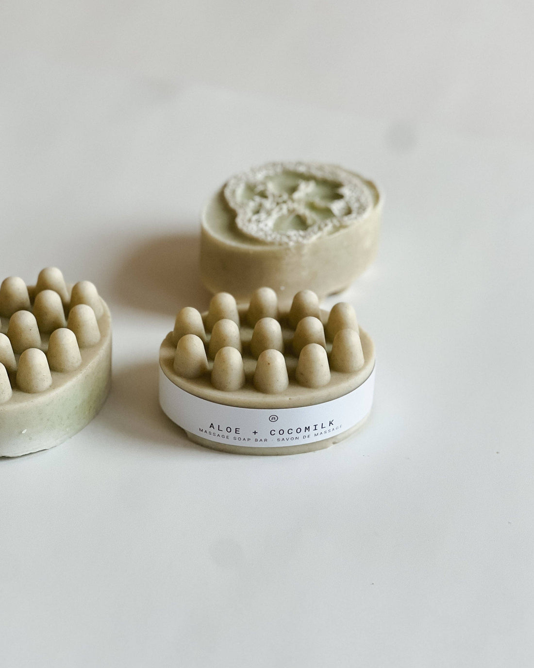 three aloe & coconut massage soap bars on a beige background showing the loofah inside the soap