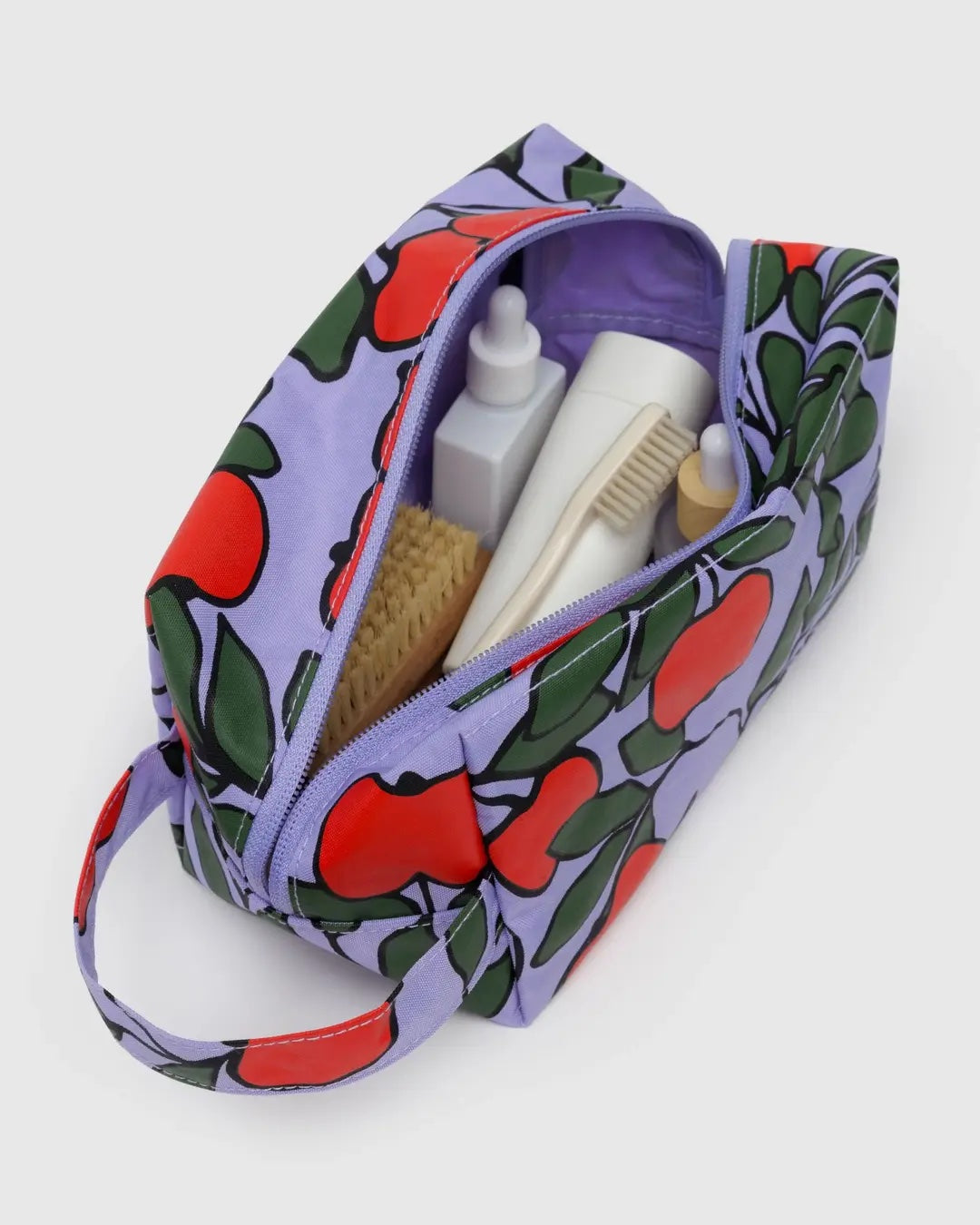 Baggu cosmetic Dopp Kit bag with red apple pattern containing toiletries on a white background