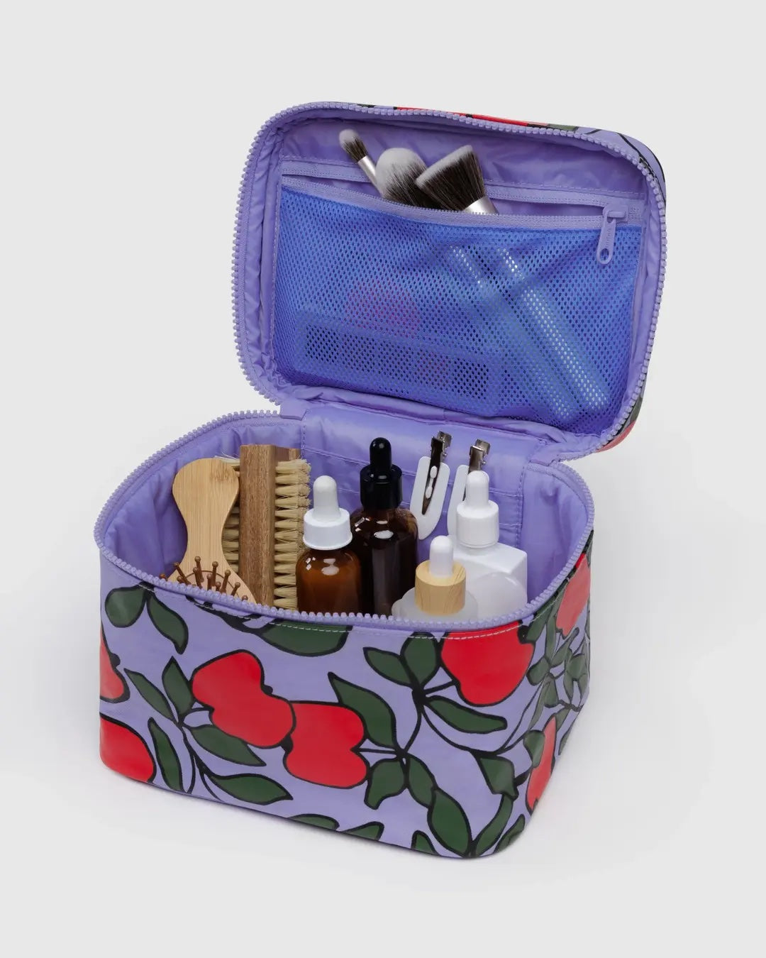 Open Baggu cosmetic case with red apple pattern on lavender background containing toiletries and beauty products on a white background