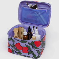 Open Baggu cosmetic case with red apple pattern on lavender background containing toiletries and beauty products on a white background