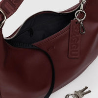detail shot of a baggu medium recycled leather crescent bag in mahogany red showing silver metal zipper and key ring hardware, matching mahogany strap and internal key lanyard