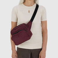 Person wearing a mahogany Baggu crossbody fanny pack bag standing in front of a white background