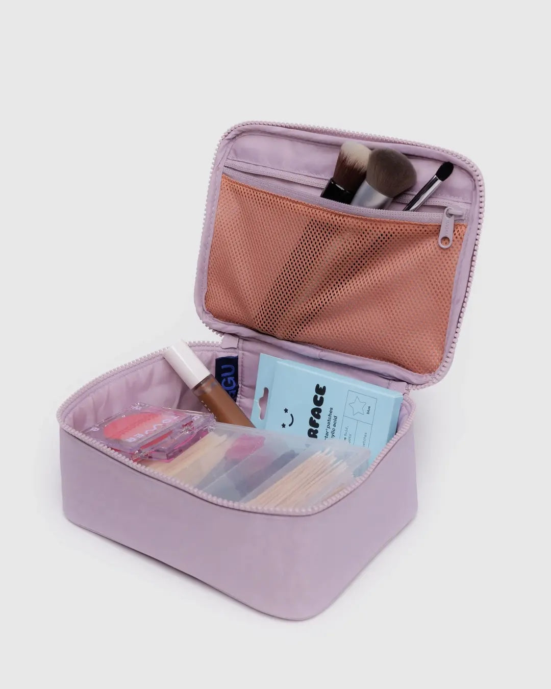 Open Baggu dusty pink cosmetic case with makeup items on a light gray background
