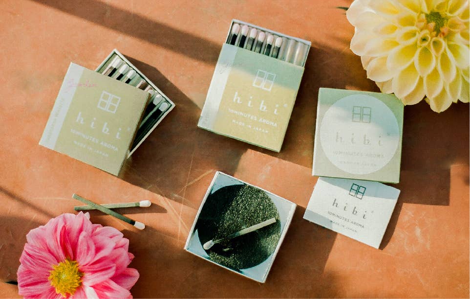 two open boxes of hibi incense matches on a terra cotta background with dahlia flowers