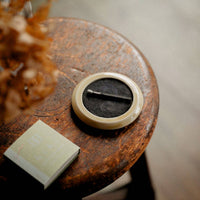 hibi yellow incense tray holding a burning incense match placed on a wooden stool with dried flowers and a pack of incense matches with a blurred floor background