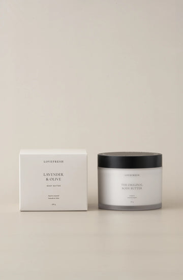 A jar of Lovefresh Lavender & Olive Body Butter next to its packaging box, with a minimalistic design in terms of color and branding.