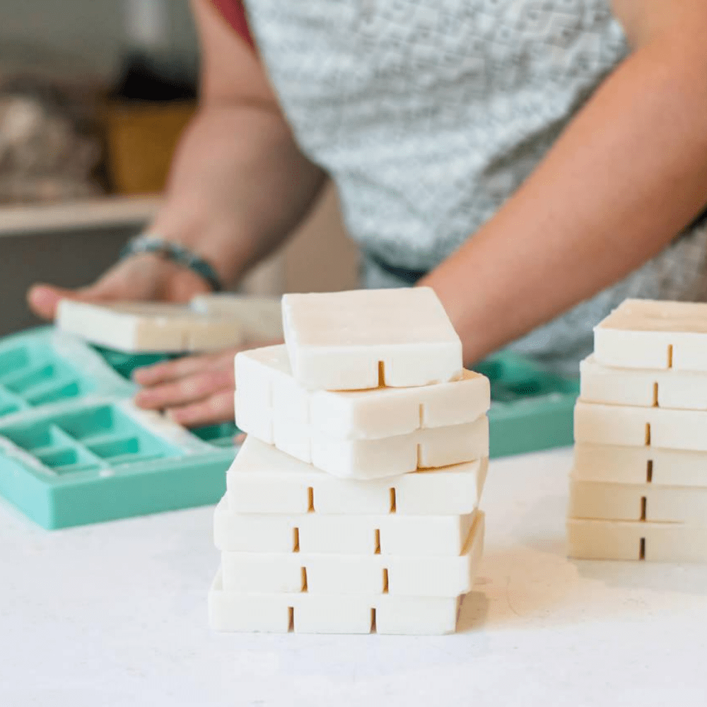 a person unmolding natural aroma wax melts which are stacked in the foreground