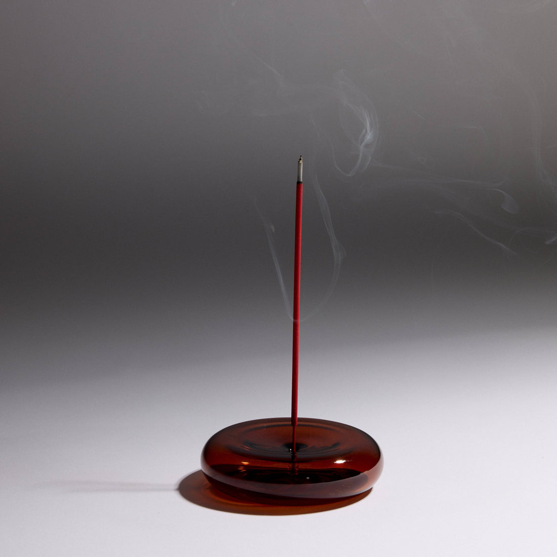 Incense burner with a single red incense stick on a gray background