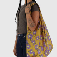 Person holding a Big Baggu yellow floral-patterned bag against a white background