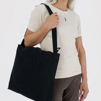 Person holding a black baggu canvas tote bag against a white background