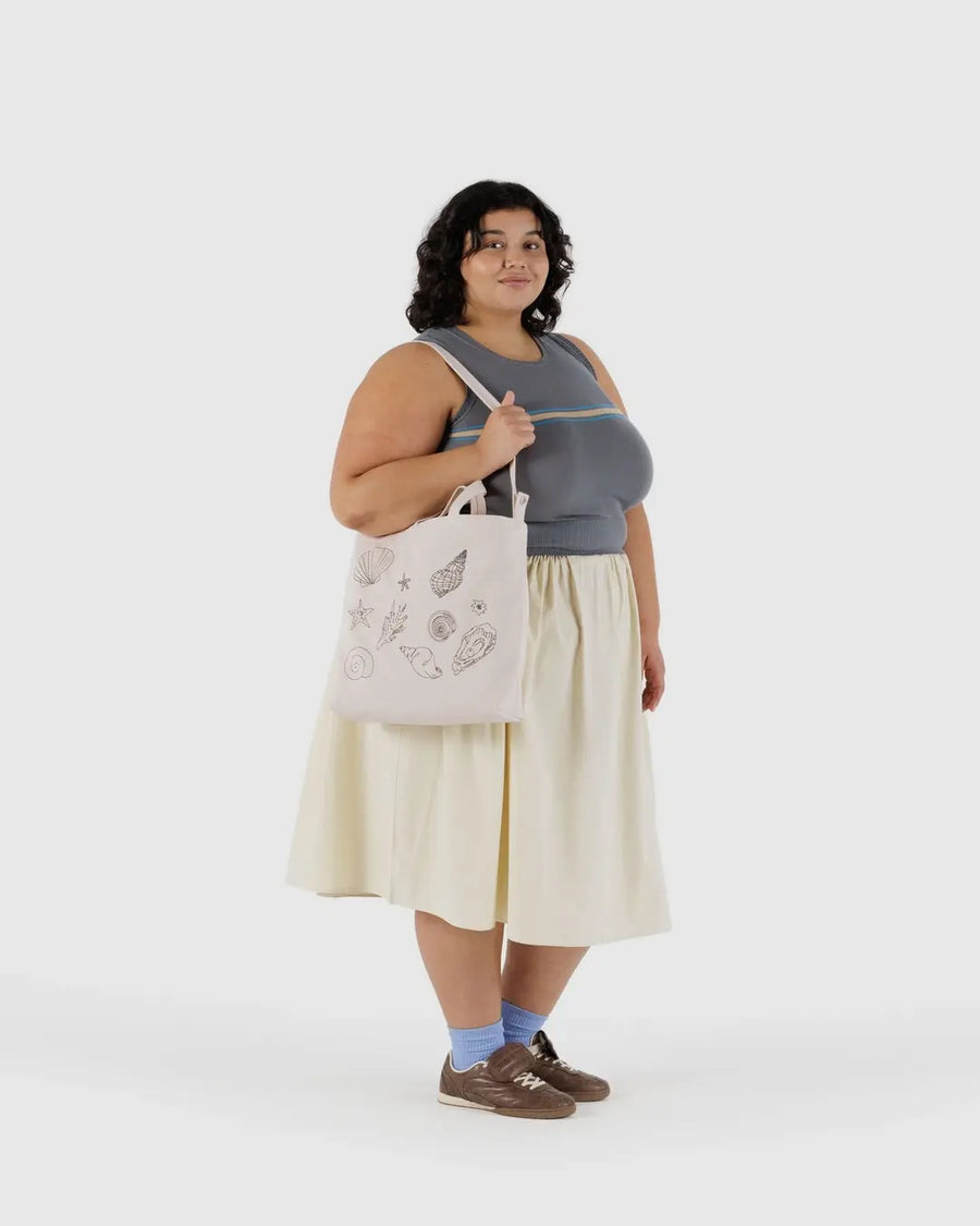 Woman holding a Baggu canvas duck bag with seashell patterned embroidery against a white background