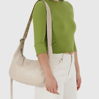Person wearing a green sweater and white pants carrying a stone leather Baggu medium crescent on their shoulder 