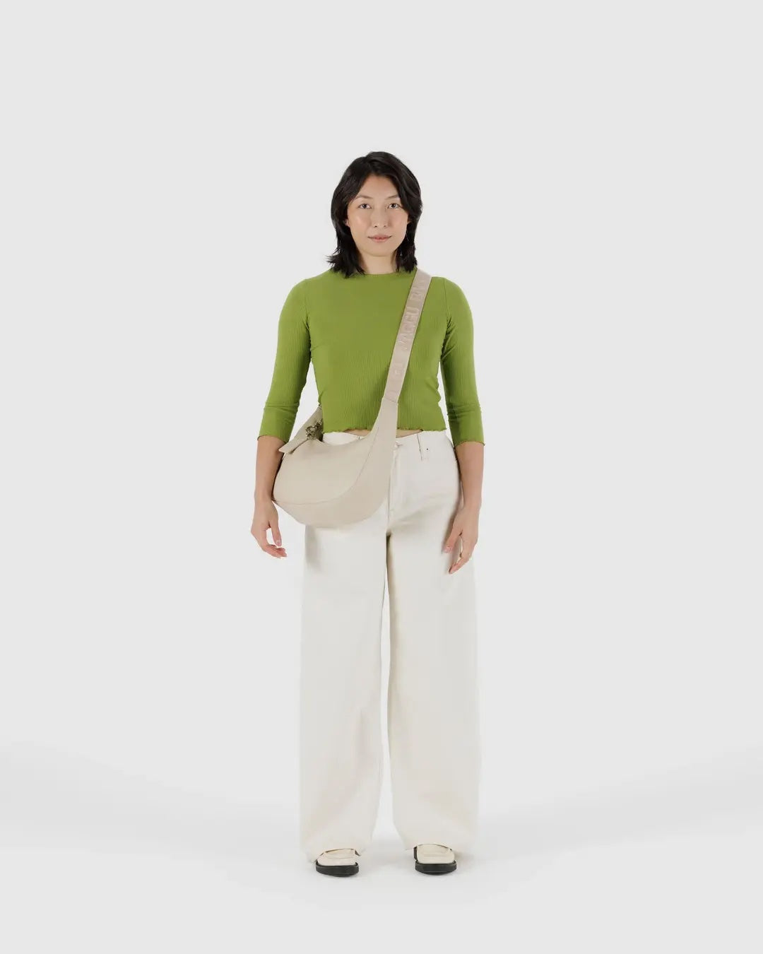 Person wearing a green top and white pants with a stone baggu leather medium crescent bag crossbody 