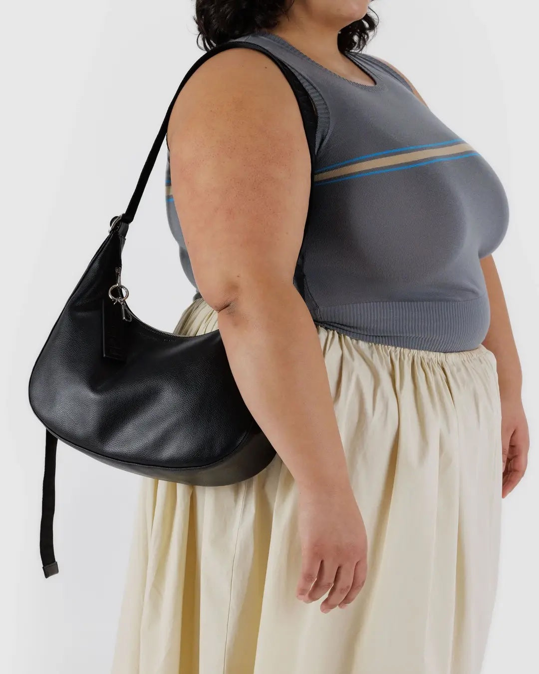 a person wearing a gray top and beige skirt, wearing a black leather baggu medium crescent bag on their shoulder 
