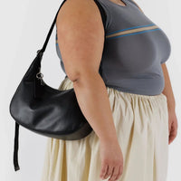 a person wearing a gray top and beige skirt, wearing a black leather baggu medium crescent bag on their shoulder 