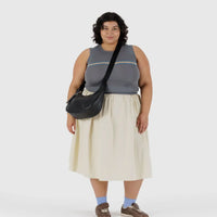 Person wearing a sleeveless top and skirt wearing a Baggu black leather crescent bag cross body on a white background