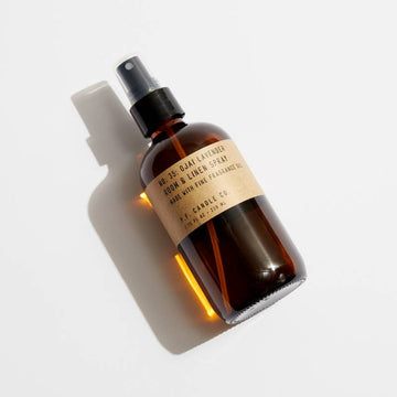 P.F. Candle Co Ojai Lavender Room & Linen Spray in an amber glass spray bottle laying on a white surface