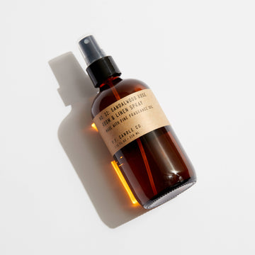 Amber glass bottle with a spray nozzle on a light gray background containing P.F. Candle Co Sandalwood Rose Room and Linen Spray