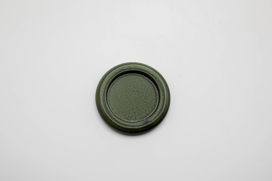 a small round green porcelain tray made for burning hibi incense matches against a white background