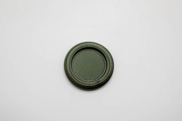 a small round green porcelain tray made for burning hibi incense matches against a white background